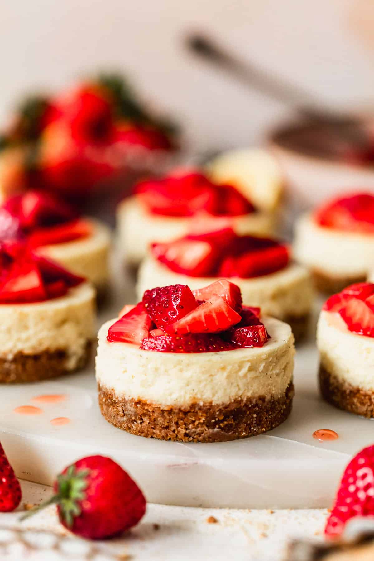 A white tray of mini strawberry cheesecakes on a pink backdrop next to strawberries.