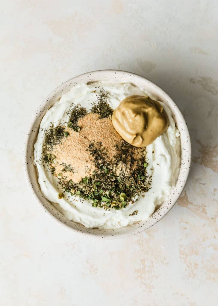 A white bowl of yogurt and herbs on a tan counter.