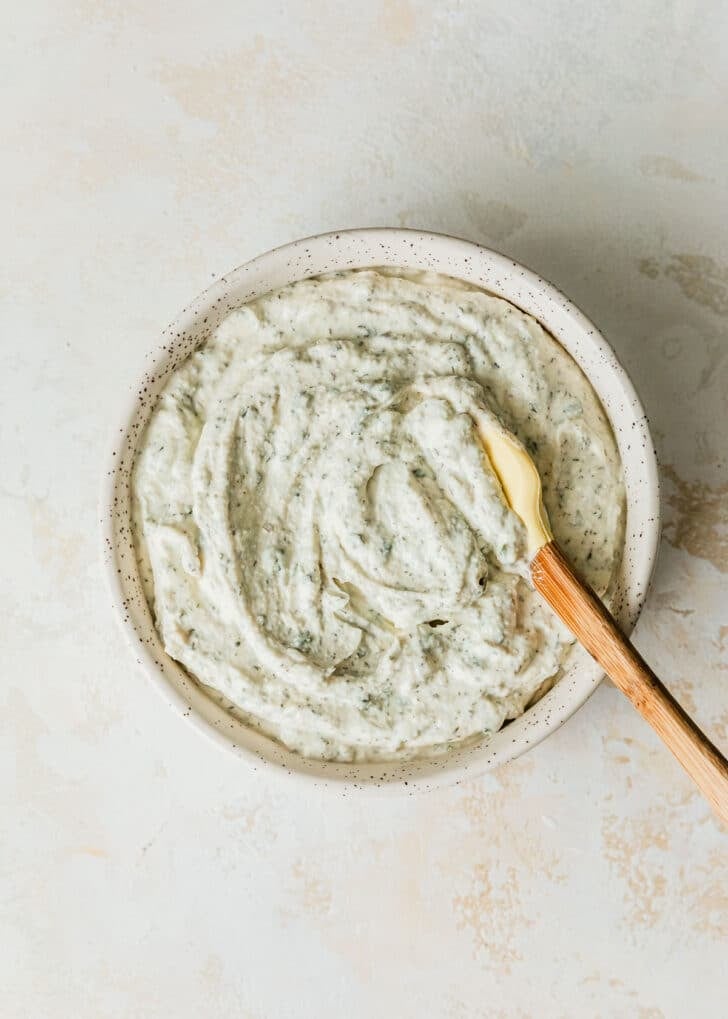 A white bowl of herb and garlic dip on a tan table.