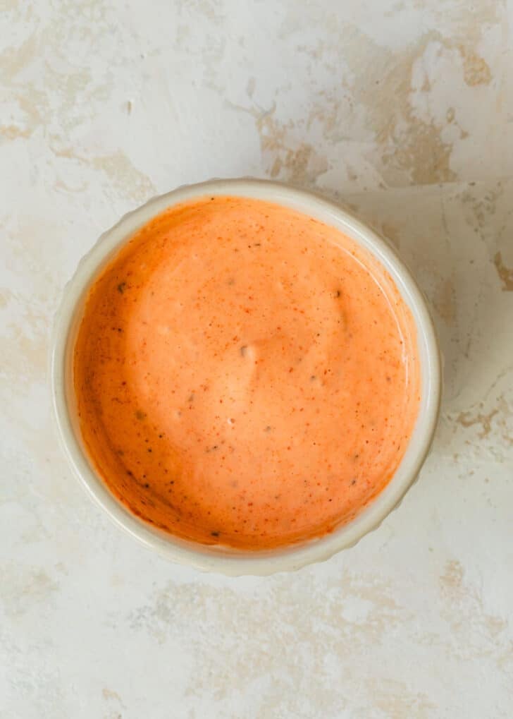 A white bowl of Sriracha ranch on a tan counter.