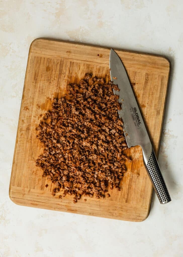 A cutting board of chopped sausage on a tan counter.
