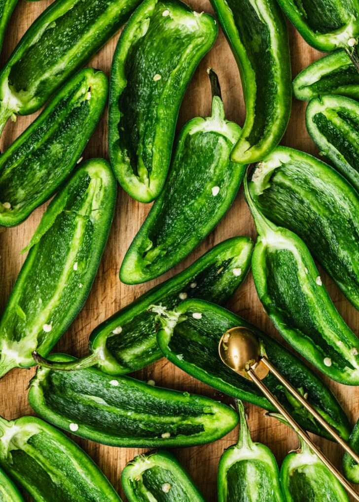 Halved jalapeños with the seeds removed on a wood board.