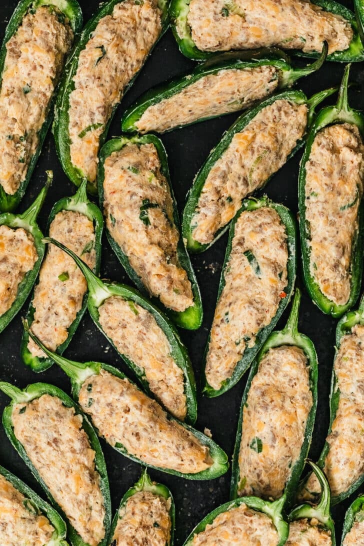Raw sausage jalapeño poppers on a black sheet pan.