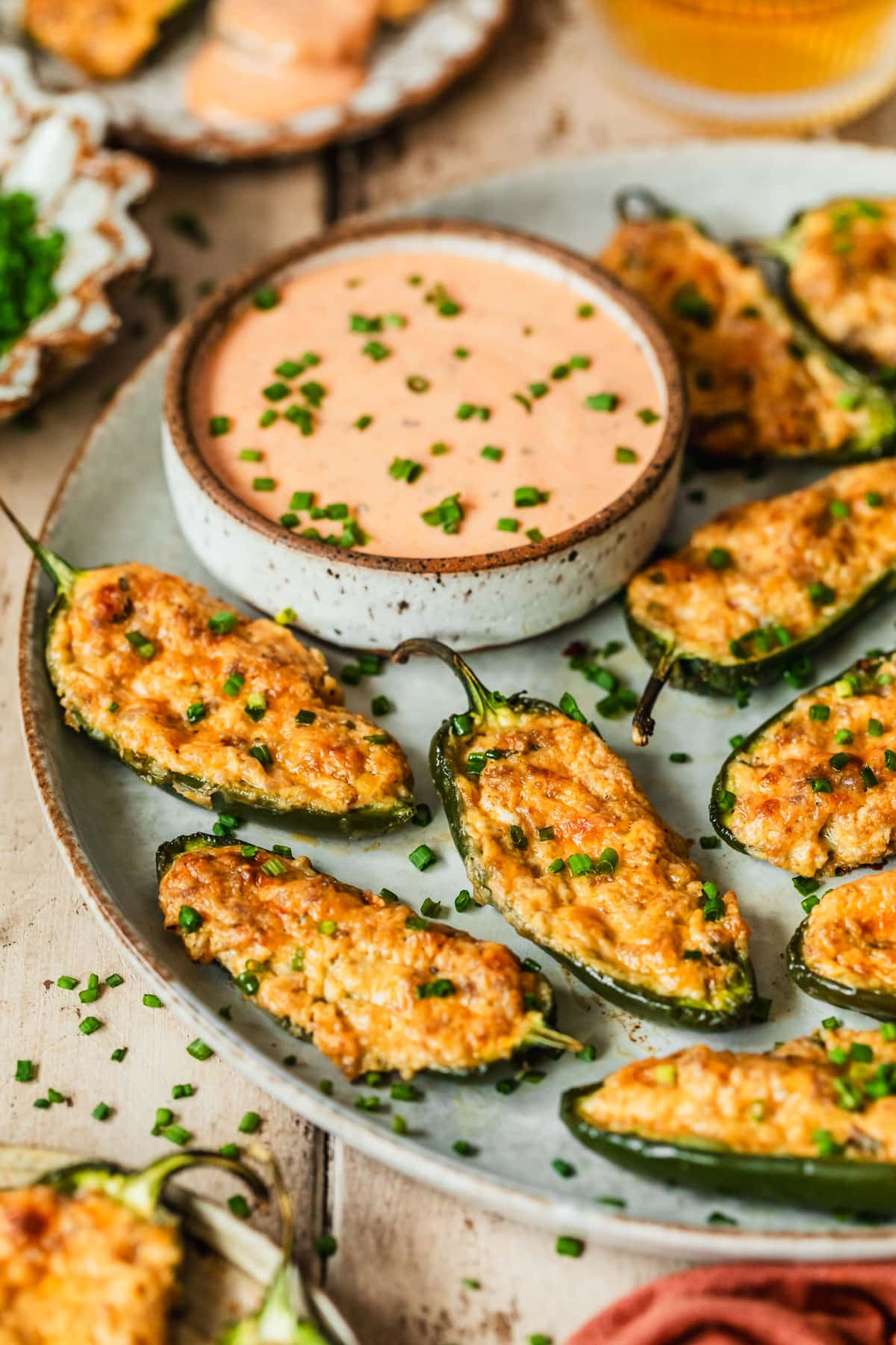 A grey tray of sausage jalapeño poppers on a wood table next to glasses of beer and brown plates of poppers.