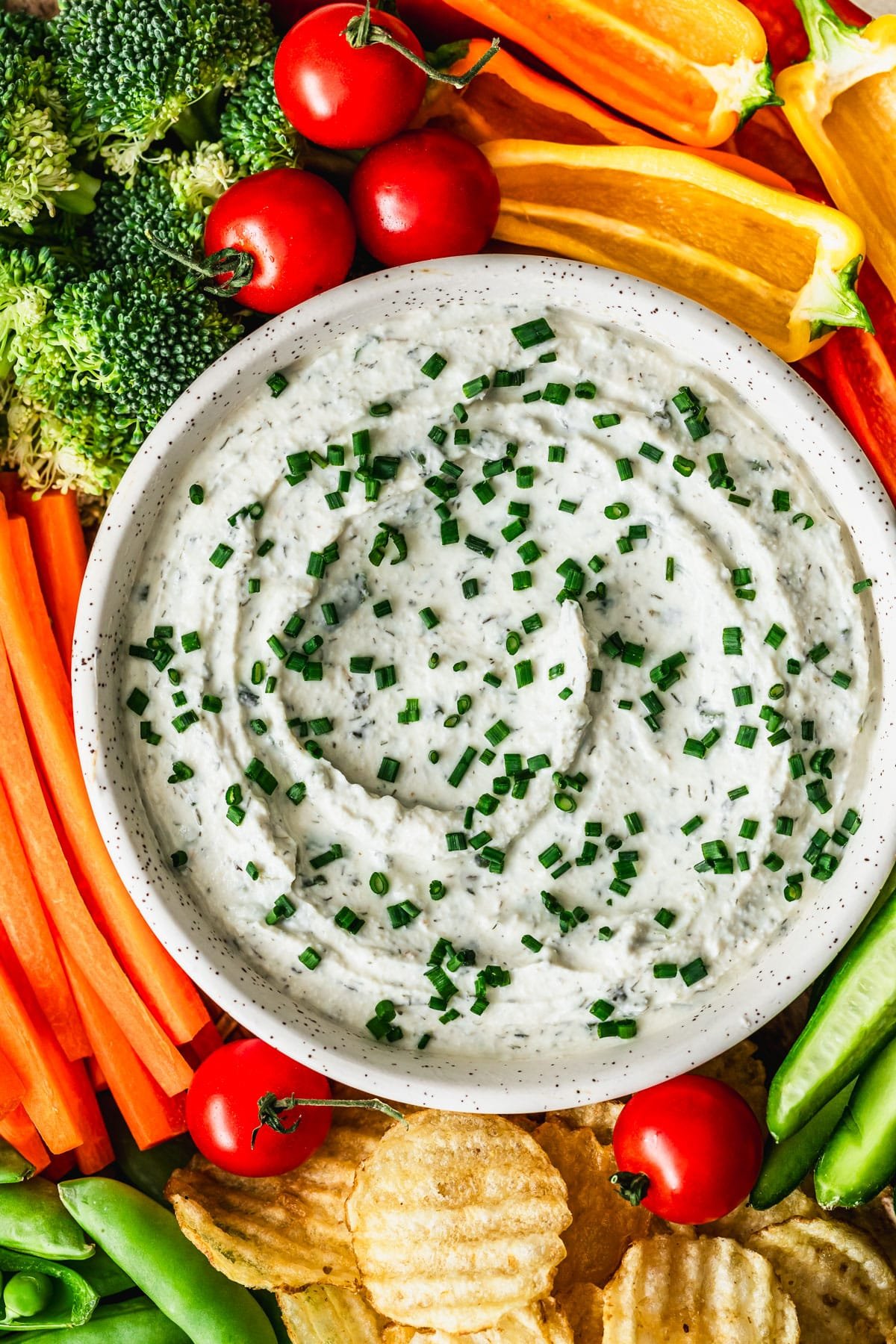 A white bowl of herb and garlic dip on a veggie tray.