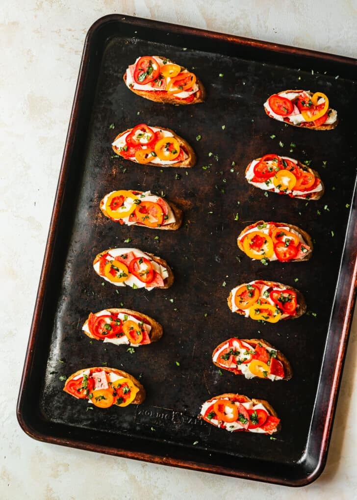 A sheet pan of toasts with cheese and veggies on a white counter.