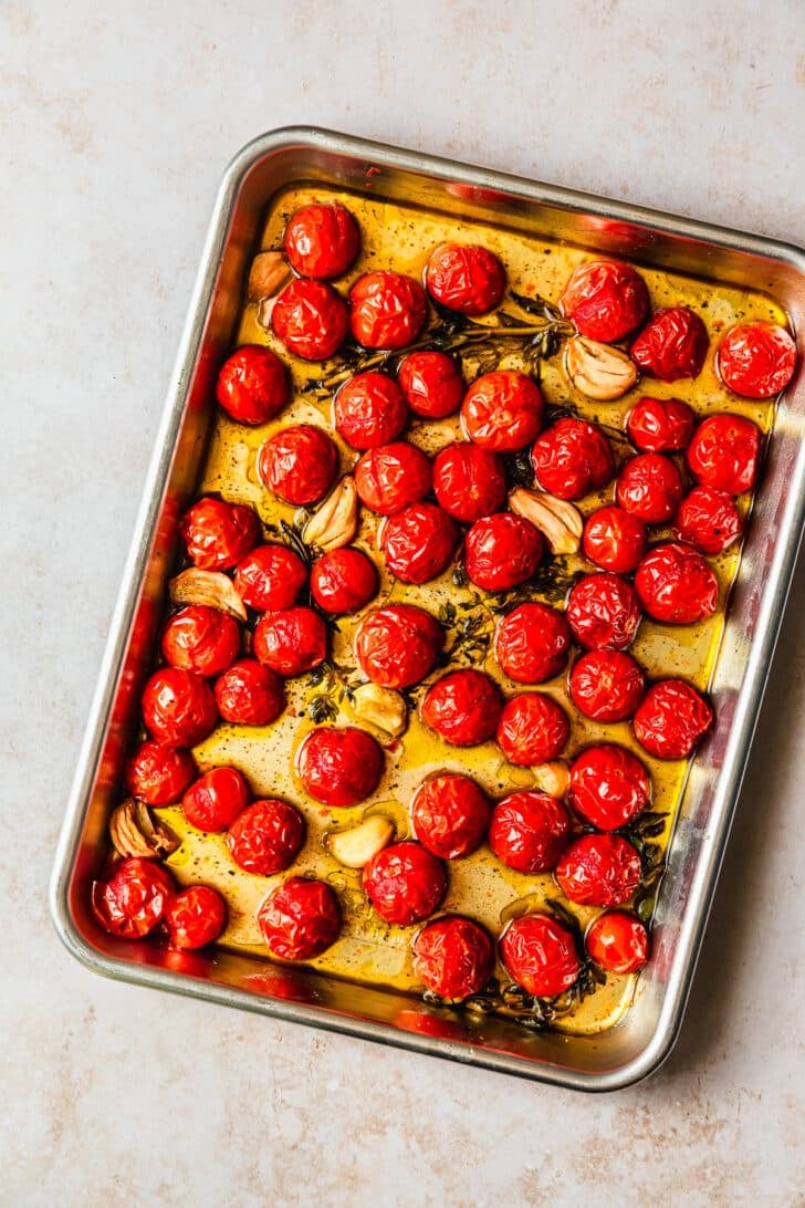 A sheet pan of roasted tomatoes on a tan counter.