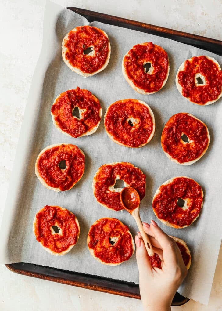 A hand spreading red sauce on bagels.