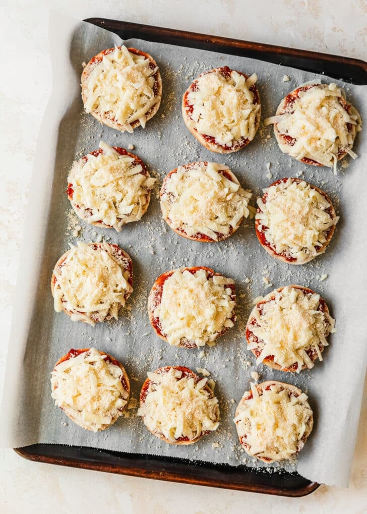 A sheet pan of mini bagels topped with cheese on a tan counter.