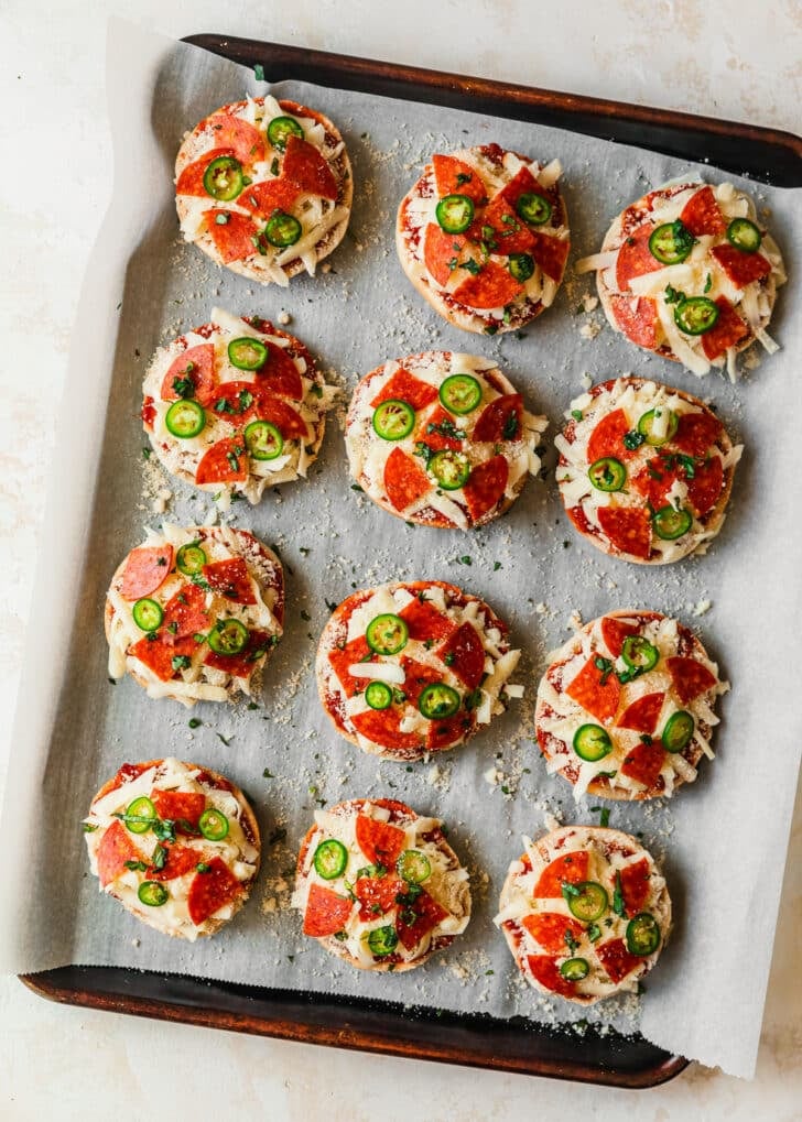 Raw homemade pizza bagel bites with pepperoni and serrano peppers on a sheet pan.
