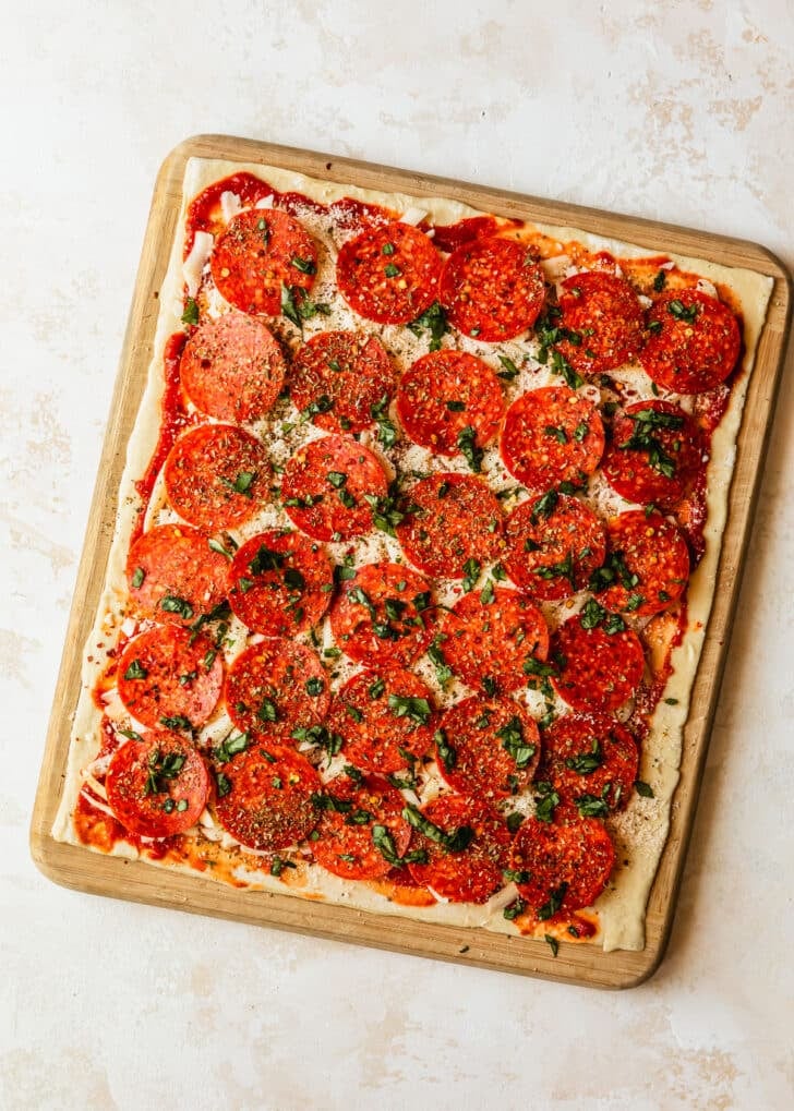 Puff pastry topped with cheese and pepperoni on a tan counter.