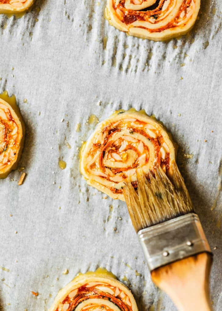 A pastry brush brushing raw pizza scrolls with egg wash.