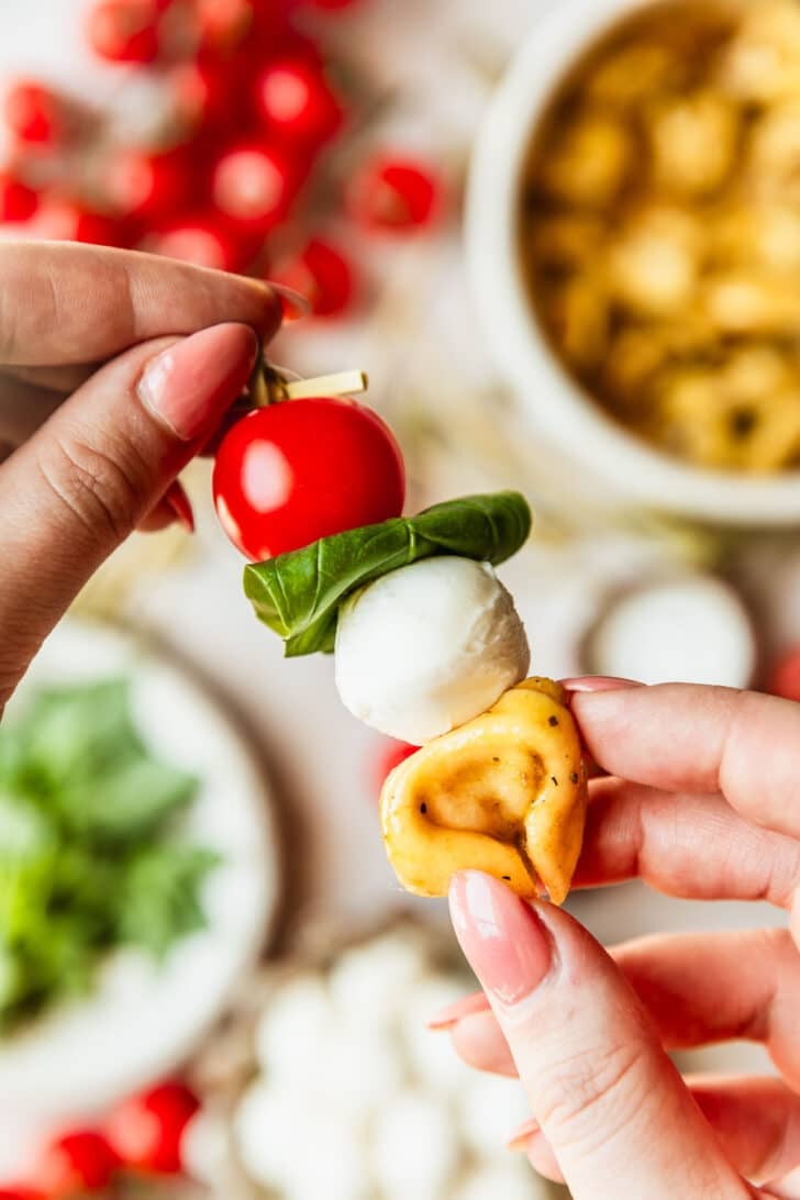Hands threading tortellini on skewers to make Caprese skewers.