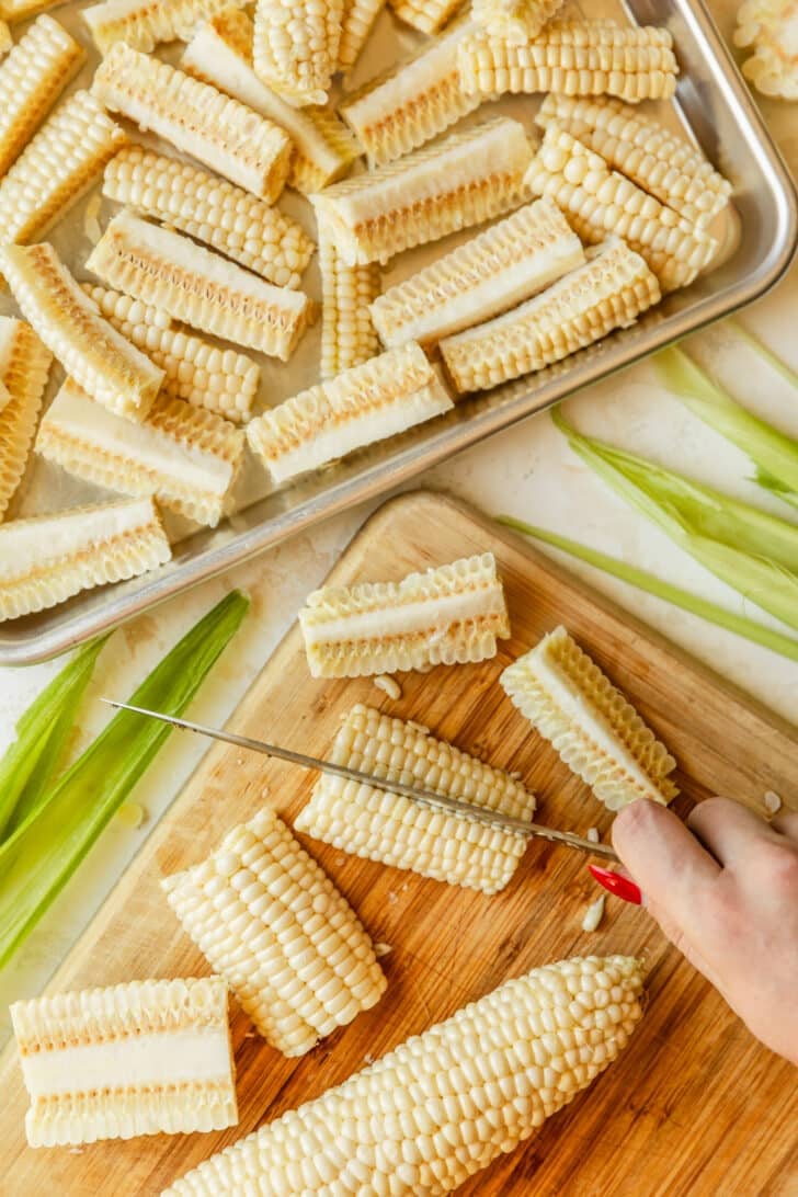 Hands using a knife to cut corn cobs into ribs.