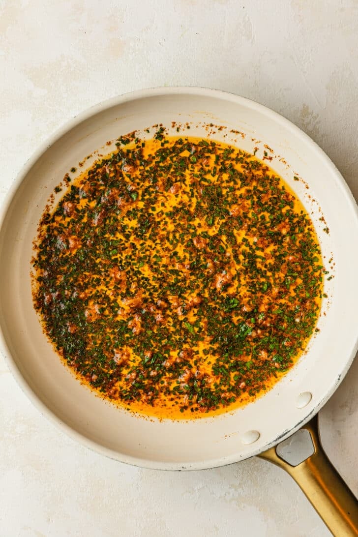 A white pan of spiced garlic butter on a tan counter.