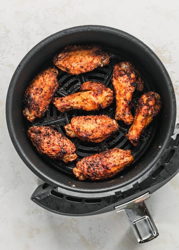 Cooked chicken wings in an air fryer on a white counter.