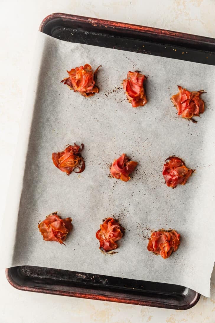 A sheet pan with piles of crispy prosciutto on a tan counter.