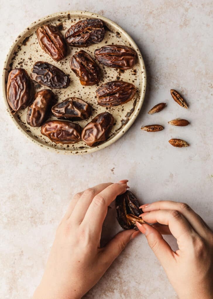 Hands removing the pit of a date on a tan counter.