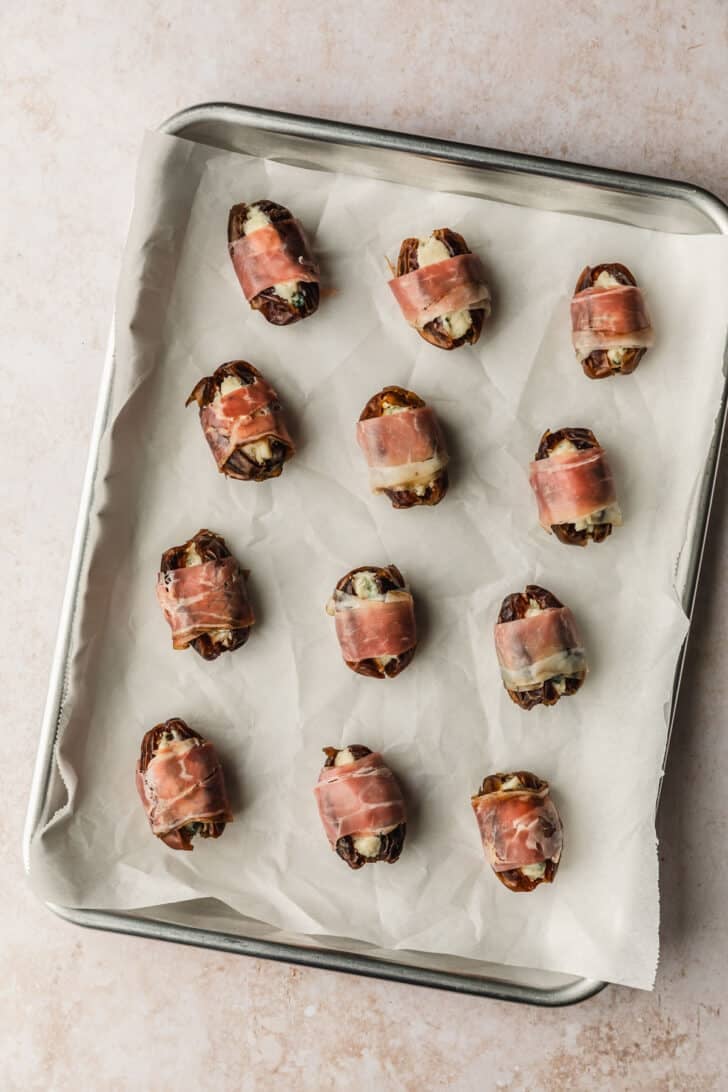 A sheet pan of prosciutto wrapped dates on a tan counter.
