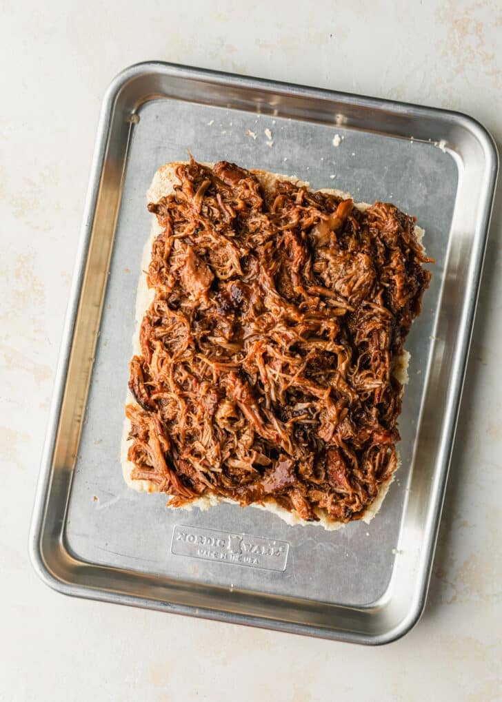A sheet pan of rolls with pulled pork on a tan counter.
