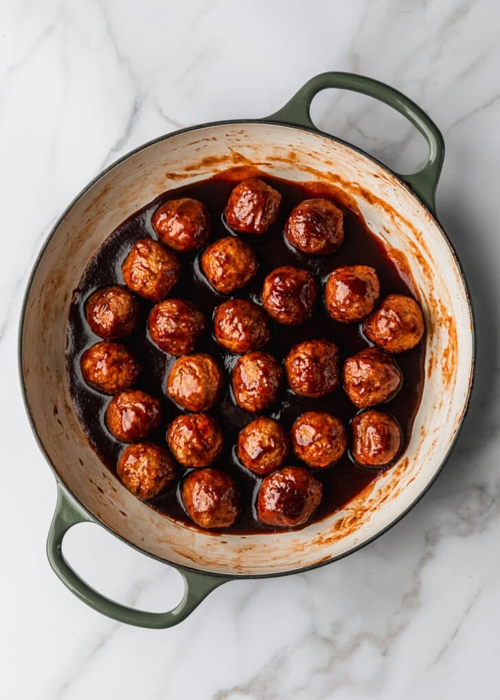A white pan of stove top BBQ grape jelly meatballs on a white table.