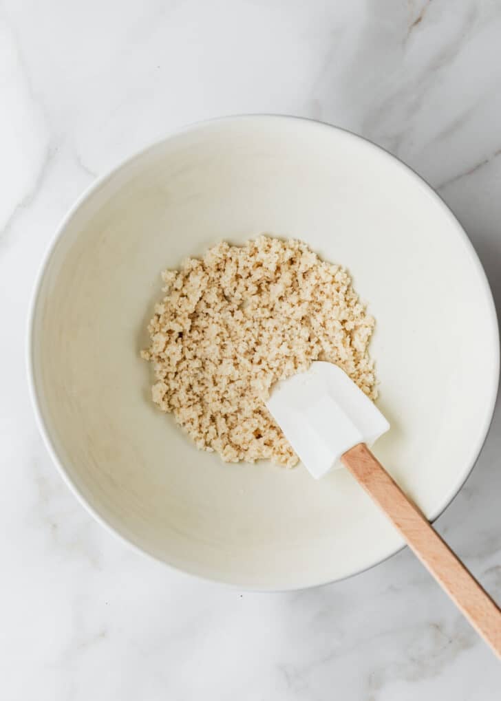 A white bowl of breadcrumbs, milk, and a rubber spatula on a white counter.