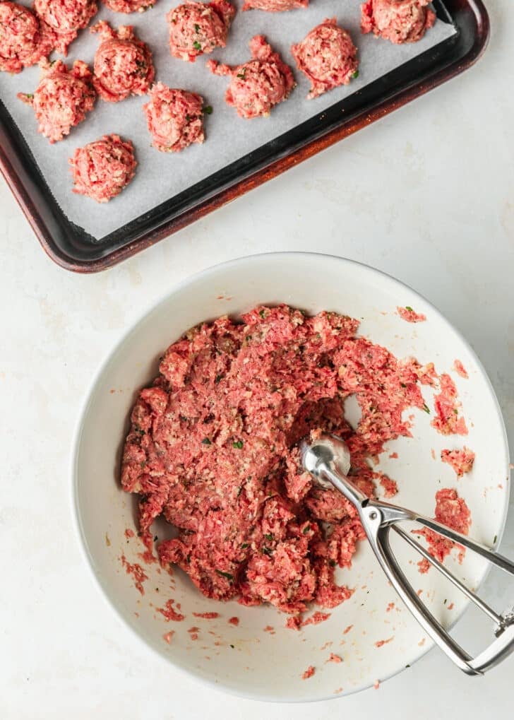 A white bowl of meat with a scoop on a white counter.