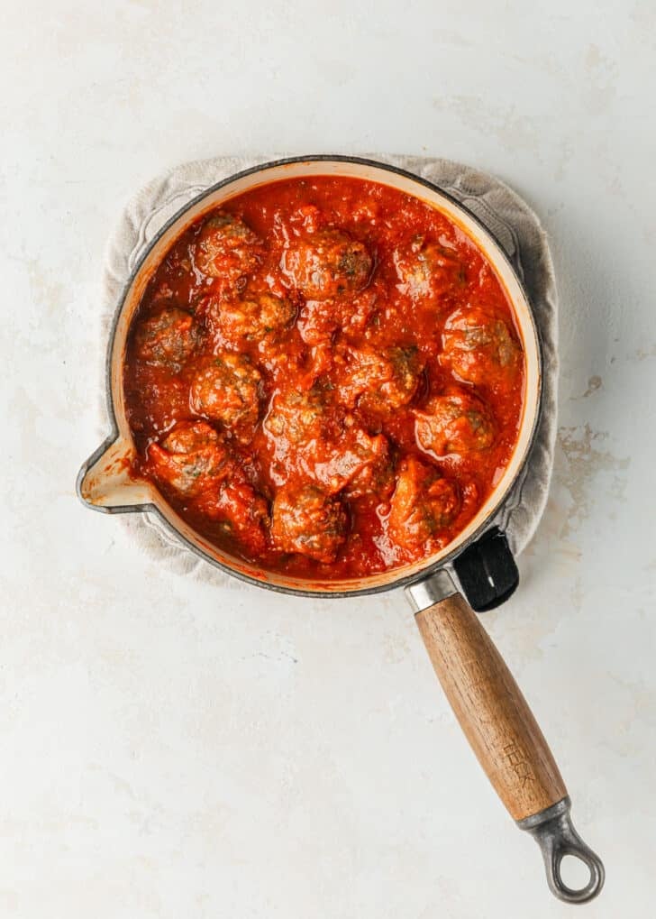 A pot of red sauce and meatballs on a tan counter.