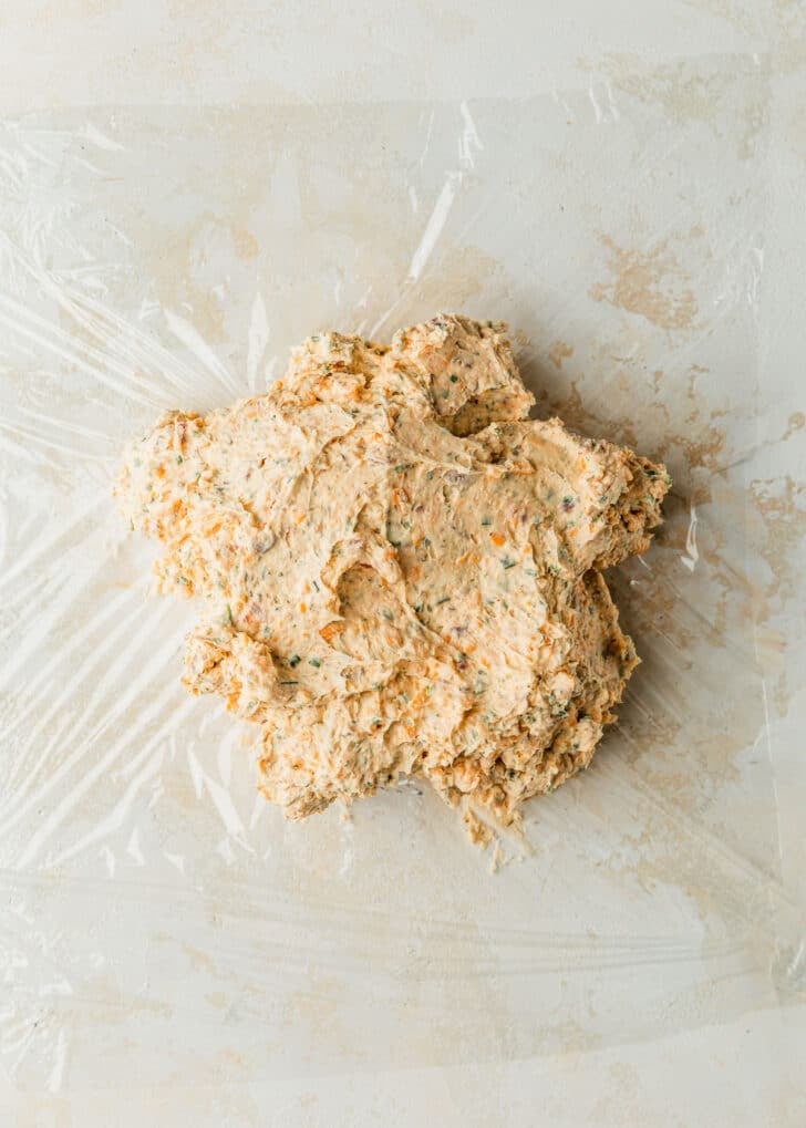 A pile of cheese mixture on a piece of plastic wrap with a tan background.