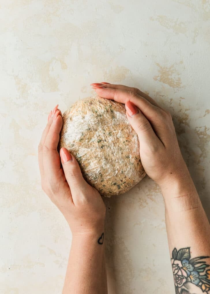 Hands shaping a pumpkin shaped cheese ball on a tan counter.