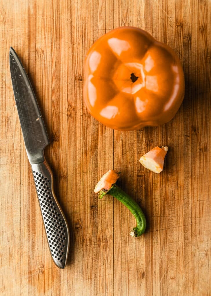 An orange bell pepper with the stem cut off on a wood board.