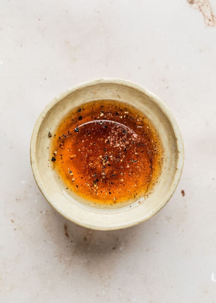A white bowl of honey, vinegar, oil, salt, and pepper on a marble counter.