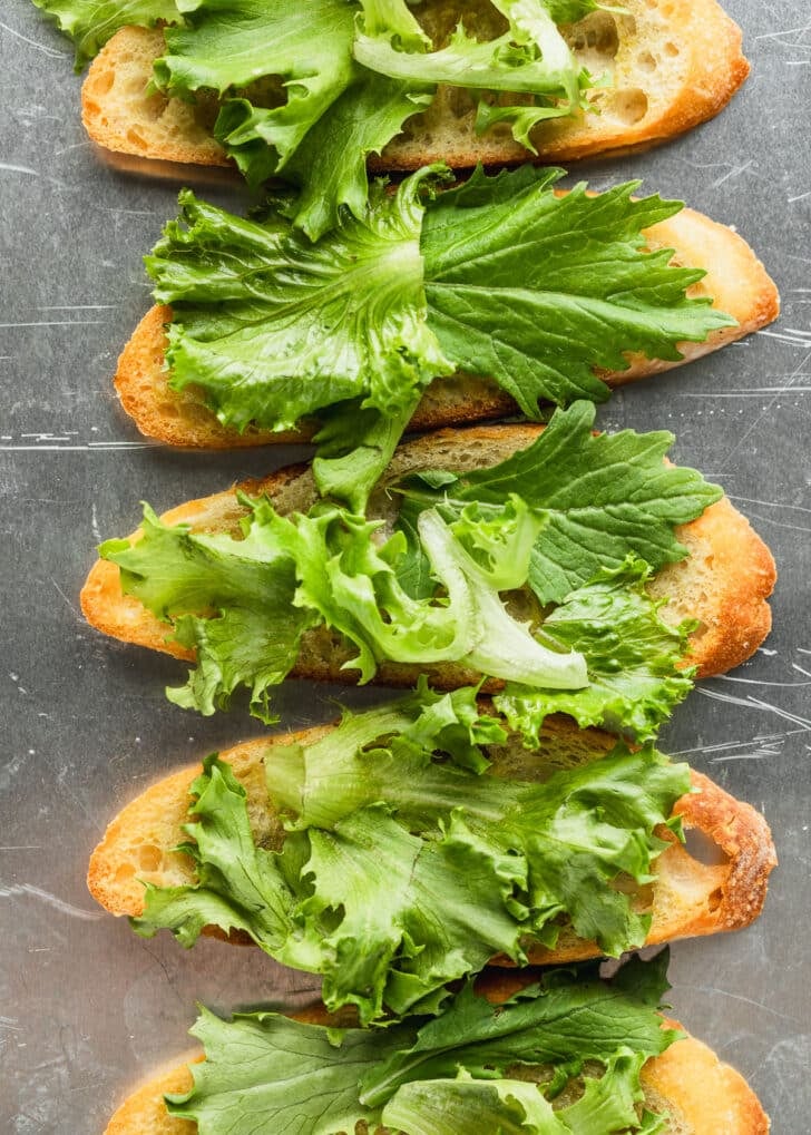 Crostini topped with lettuce on a silver pan.