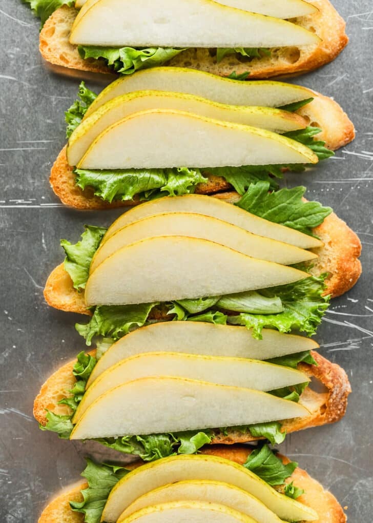 A silver pan of crostini with lettuce and pears.