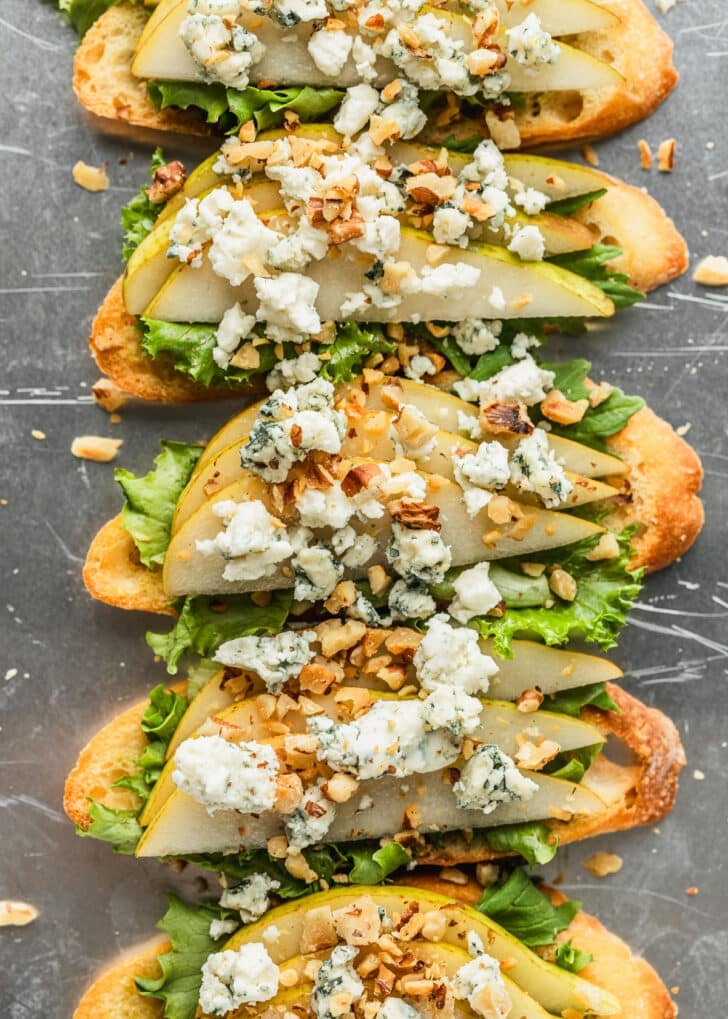 A silver pan of crostini topped with lettuce, pears, blue cheese, and walnuts.