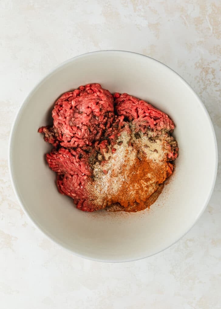 A white bowl of ground beef and spices on a tan counter.
