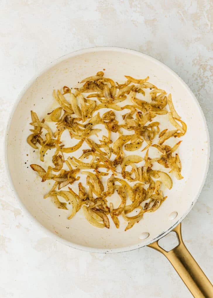 A white pan of sauteed onions on a tan table.