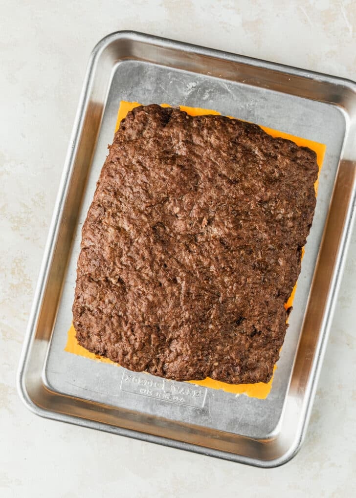 A sheet pan of unbaked cheeseburger sliders on Hawaiian rolls.