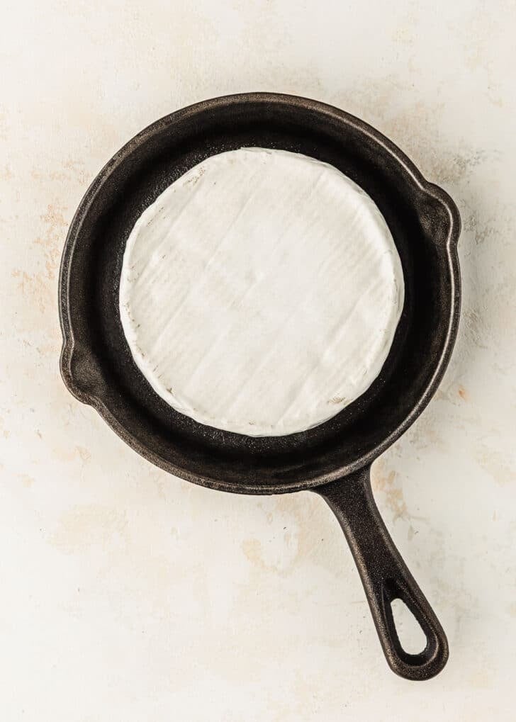 A cast iron skillet with brie on a tan counter.