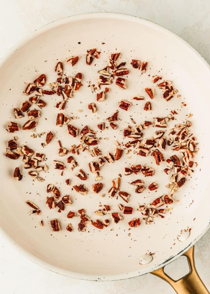 A white pan of pecans on a beige table.
