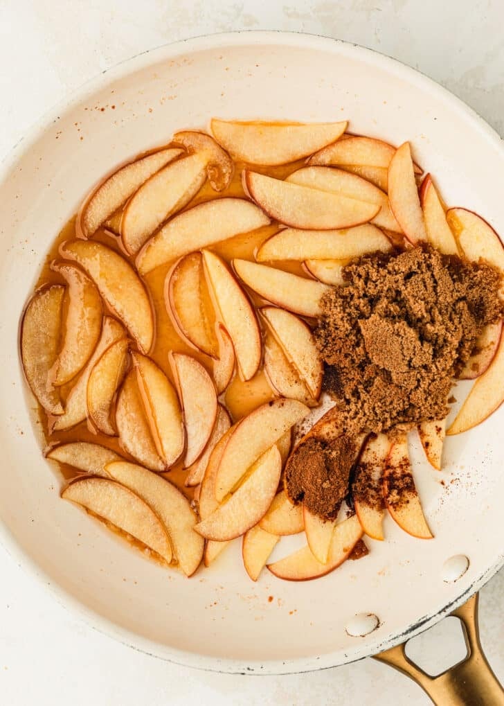 A white pan of apples, brown sugar, and maple syrup on a tan counter.