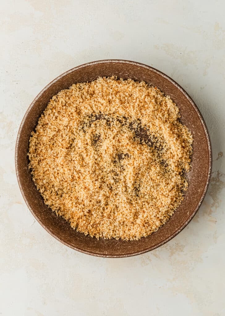 A brown bowl of Panko breadcrumbs and parmesan on a tan counter.