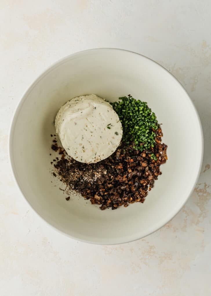 A white bowl of Boursin cheese, mushrooms, shallots, and chives.