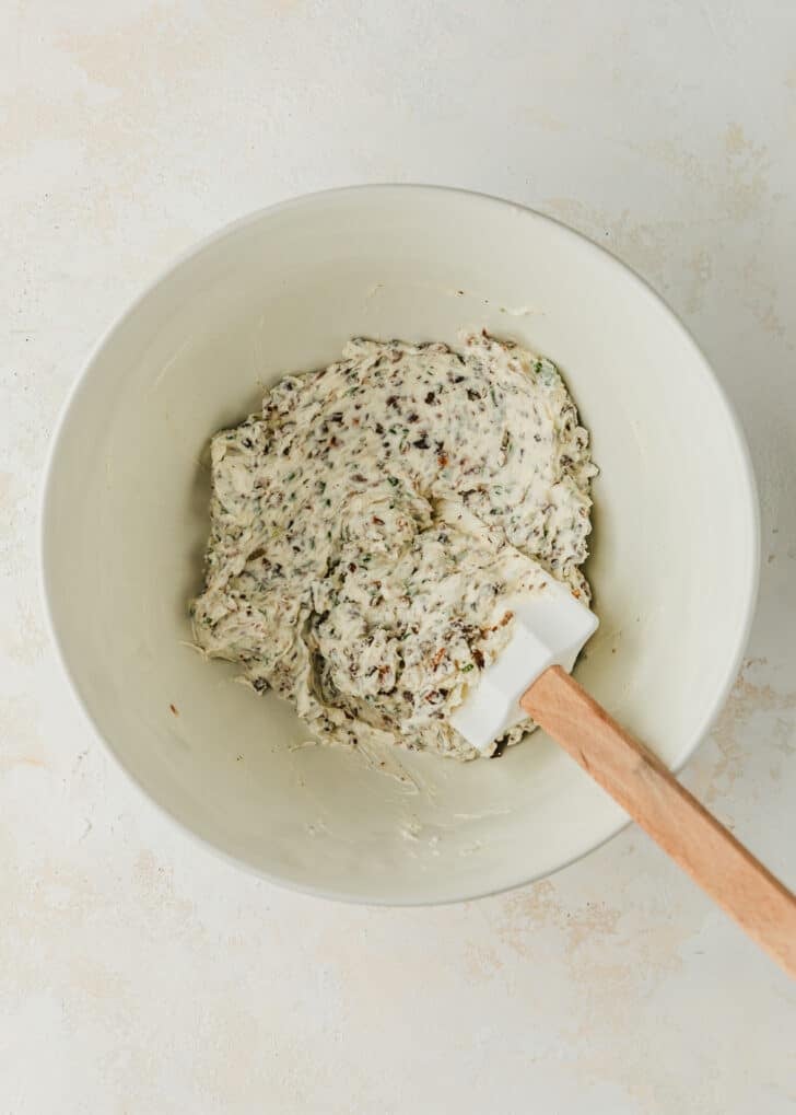 A white bowl of Boursin cheese mixed with mushrooms, shallots, and chives.