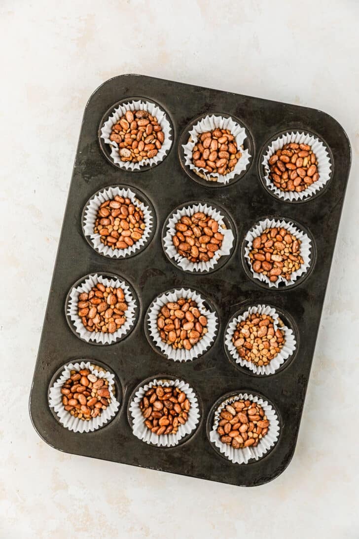 Muffin tins with pie crust, parchment paper, and pie weights on a tan counter.