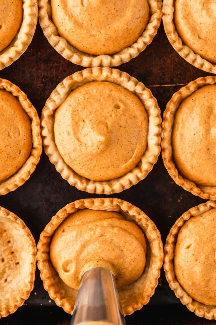 A piping bag assembling mini pumpkin cream cheese pies on a sheet pan.