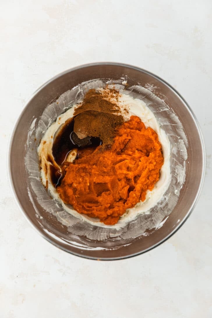 A silver bowl of cream cheese, pumpkin, spices, and vanilla on a beige table.