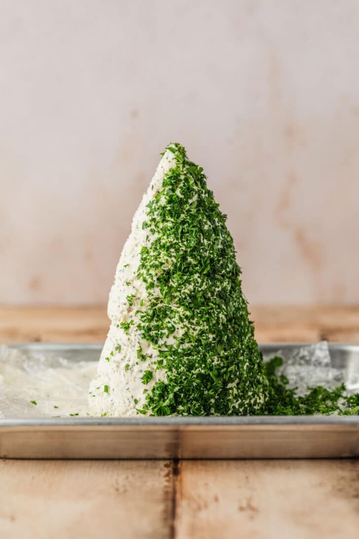 A cone of cheese covered in parsley on a wood table.