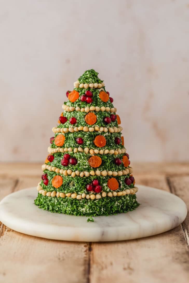A marble board with a Christmas tree cheese ball on a wood table.