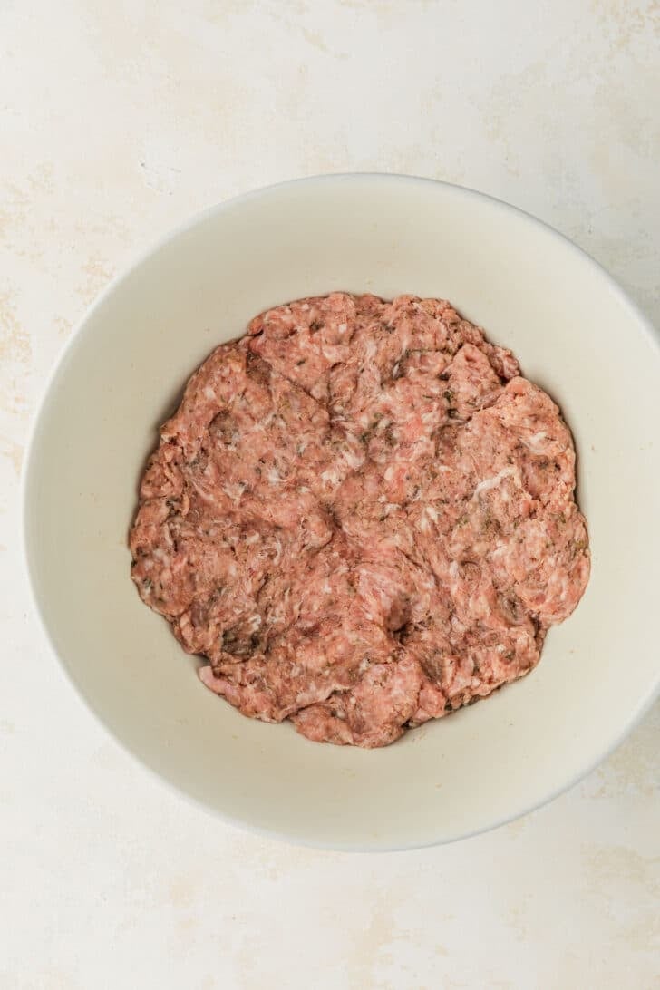 A white bowl of pork sausage on a tan counter.